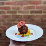 circa scotch egg on a white plate with brick wall behind it