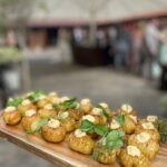 circa mini baked potato hassleback style on a wooden board overlooking a courtyard